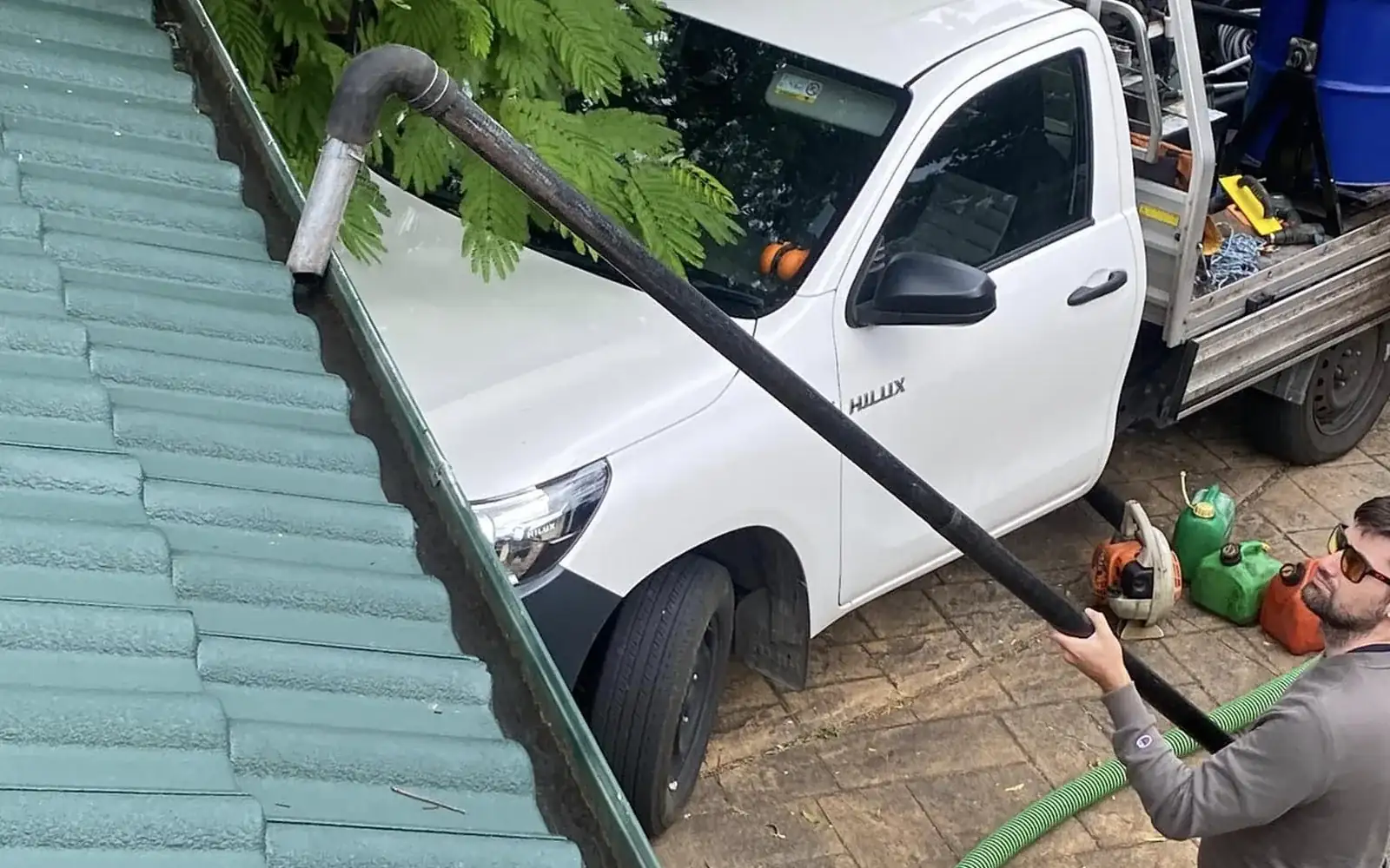 Gutter cleaning in Nowra by Ed's Property Maintenance, vacuum hose running from the ute up to the roof