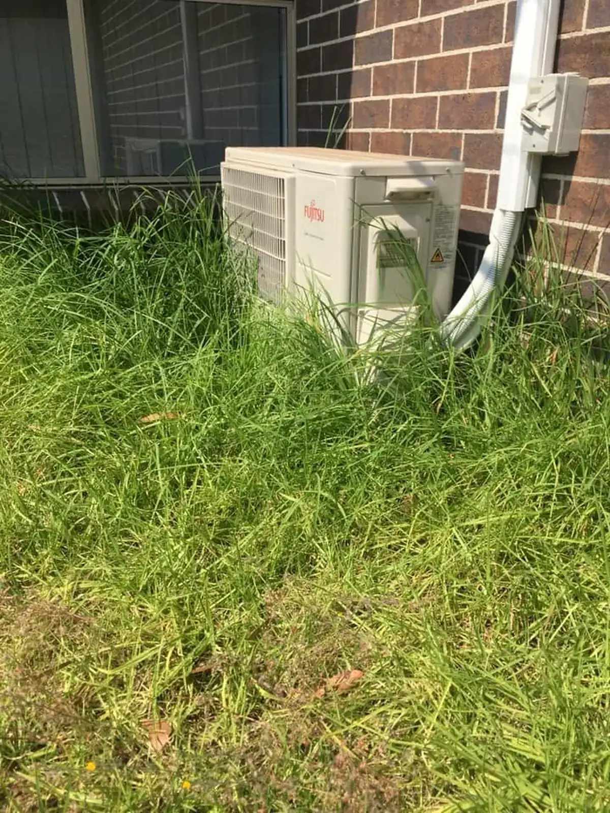 Overgrown grass around an air conditioning unit before property maintenance